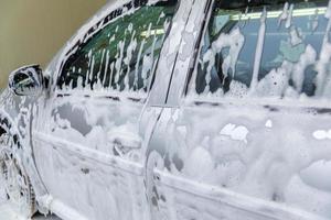 een auto gedekt door zeep schuim terwijl het wassen binnenshuis - detailopname met selectief focus foto