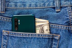 ons dollar bankbiljetten en groen smartphone in de links achterzijde zak- van blauw jeans. foto
