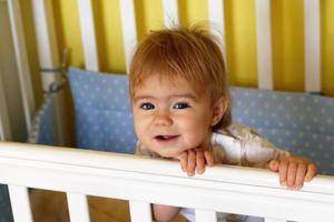 gelukkig een jaar oud meisje met blauw ogen en blond na ontwaken omhoog in de ochtend- in haar bed. foto