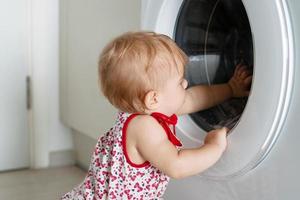 weinig meisje is op zoek in het wassen machine. foto