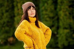 mooi Europese brunette gekleed in een geel wollen trui en hoed buiten. de mooi meisje wie draagt dik elegant herfst kleren in koel het weer. foto