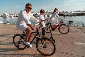 gelukkig familie genieten van een mooi ochtend- door de zee samen, ouders rijden een fiets en hun zoon rijden een elektrisch scooter. selectief focus foto