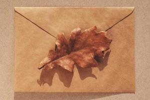 eik blad Aan bruin papier envelop, minimaal vallen achtergrond, herfst vlak leggen foto