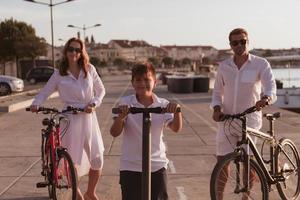 gelukkig familie genieten van een mooi ochtend- door de zee samen, ouders rijden een fiets en hun zoon rijden een elektrisch scooter. selectief focus foto