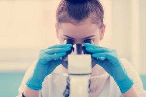 vrouw leerling wetenschapper op zoek door een microscoop foto