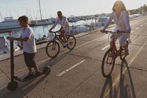 gelukkig familie genieten van een mooi ochtend- door de zee samen, ouders rijden een fiets en hun zoon rijden een elektrisch scooter. selectief focus foto