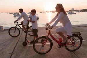 gelukkig familie genieten van een mooi ochtend- door de zee samen, ouders rijden een fiets en hun zoon rijden een elektrisch scooter. selectief focus foto
