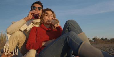 liefhebbend jong paar zittend Aan de strand naast kampvuur drinken bier foto