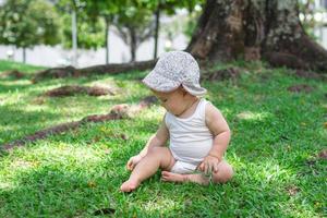 weinig baby meisje in wit kleding en Panama is spelen met bloemen Aan gras in park Bij zomer. kind onderzoekt wereld in de omgeving van. foto