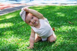 levensstijl portret van glimlachen baby meisje in wit kleding en Panama. kind spelen Aan gras Aan een zonnig zomer dag. foto