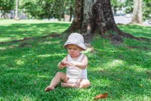 aanbiddelijk baby meisje in wit kleding en Panama is spelen met droog geel bladeren Aan gras. zomer zonnig dag in park. foto