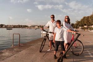 gelukkig familie genieten van een mooi ochtend- door de zee samen, ouders rijden een fiets en hun zoon rijden een elektrisch scooter. selectief focus foto