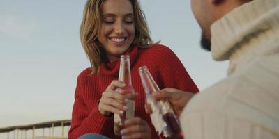 liefhebbend jong paar zittend Aan de strand naast kampvuur drinken bier foto