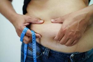 overgewicht aziatische vrouw gebruikt hand om dikke buik te knijpen groot formaat overgewicht en obesitas. foto