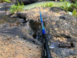klein blauw en zwart visvangst hengel Aan een rots klaar voor visvangst foto