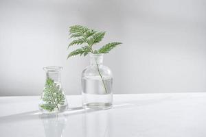 Doorzichtig water in glas fles en flacon met natuurlijk groen vertrekken in biotechnologie wetenschap laboratorium achtergrond foto