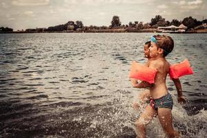 zorgeloos jongens hebben pret terwijl rennen door zee in zomer dag. foto