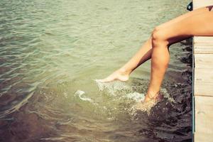 onherkenbaar vrouw spatten water terwijl ontspannende Aan een pier. foto