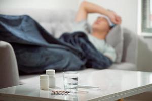 ziek verspild Mens aan het liegen in sofa lijden verkoudheid en winter griep virus hebben geneeskunde tablets in Gezondheid zorg concept op zoek temperatuur Aan thermometer foto