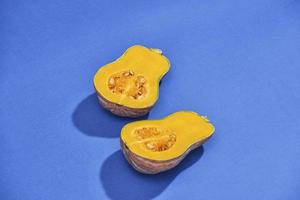 twee helften van rijp butternut squash pompoen Aan een blauw achtergrond. oranje pompoen met een staart. detailopname foto