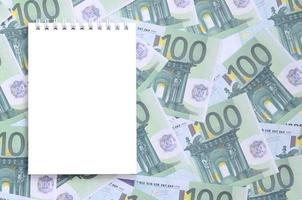 wit notitieboekje met schoon Pagina's aan het liegen Aan een reeks van groen monetair denominaties van 100 euro. een veel van geld vormen een eindeloos hoop foto