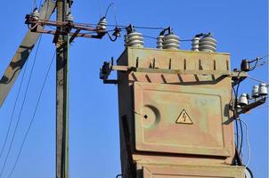 oud en verouderd elektrisch transformator tegen de achtergrond van een wolkenloos blauw lucht. apparaat voor distributie van levering van hoog voltage energie foto