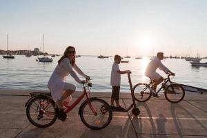 gelukkig familie genieten van een mooi ochtend- door de zee samen, ouders rijden een fiets en hun zoon rijden een elektrisch scooter. selectief focus foto