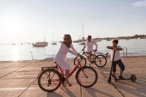 gelukkig familie genieten van een mooi ochtend- door de zee samen, ouders rijden een fiets en hun zoon rijden een elektrisch scooter. selectief focus foto