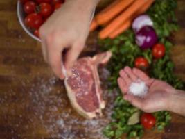 chef zetten zout Aan sappig plak van rauw steak foto