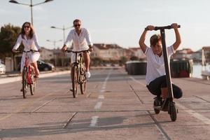 gelukkig familie genieten van een mooi ochtend- door de zee samen, ouders rijden een fiets en hun zoon rijden een elektrisch scooter. selectief focus foto