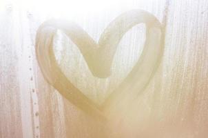 een hartvormig tekening getrokken door een vinger Aan een beneveld glas in regenachtig weer foto
