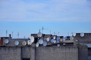 een veel van satelliet televisie antennes Aan de op het dak onder een blauw lucht foto