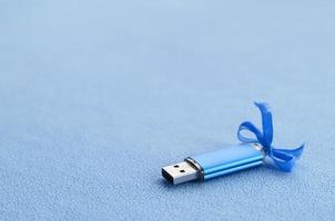 briljant blauw USB flash geheugen kaart met een blauw boog leugens Aan een deken van zacht en harig licht blauw fleece kleding stof. klassiek vrouw geschenk ontwerp voor een geheugen kaart foto