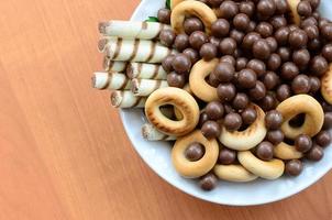 krokant buisjes, chocola smelten ballen en bagels liggen in een wit bord Aan een houten tafel. mengen van divers snoepgoed foto