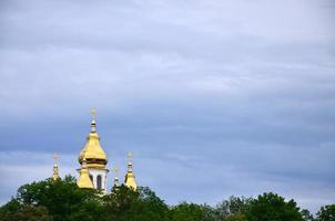 gouden koepels van een orthodox kerk tussen bloeiende bomen tegen een achtergrond van een bewolkt blauw lucht foto