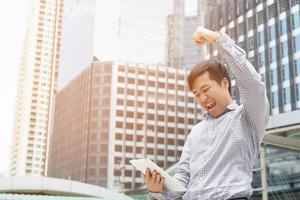 investeerder jong zakenman staand gebruik makend van een laptop tablet en houdt een vuist winnen voorraad markt voorraad emotioneel omhoog heel gelukkig humeur krijgen winst. foto