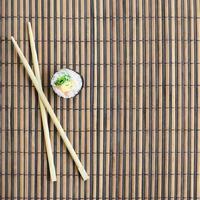 sushi rollen en houten eetstokjes liggen Aan een bamboe rietje naaien mat. traditioneel Aziatisch voedsel. top visie. vlak leggen minimalisme schot met kopiëren ruimte foto