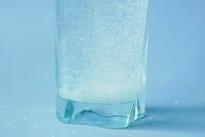 gieten wit suiker in een glas van water Aan blauw achtergrond foto