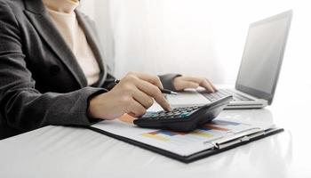 vrouw ondernemer gebruik makend van een rekenmachine met een pen in haar hand, berekenen financieel kosten Bij huis kantoor foto