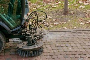 de gemeentelijk onderhoud voert seizoensgebonden werk in de park. de veger picks omhoog een veel van brokstukken. de borstels vegen de asfalt foto