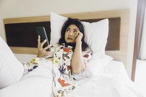 verdrietig jong vrouw huilen van de bed. houden de smartphone typen. foto