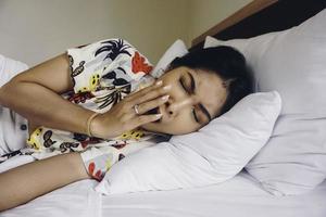 een jong Aziatisch vrouw Aan de bed voelt slaperig, ze is aan het liegen Aan de kant en geeuwen foto