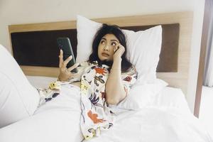 verdrietig jong vrouw huilen van de bed. houden de smartphone typen. foto