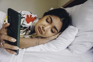 verdrietig jong vrouw fronsen van de bed aan het wachten voor een telefoontje terwijl Holding de smartphone. foto