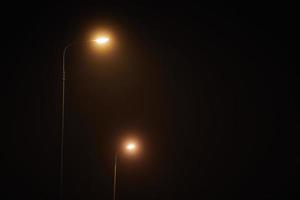 twee nacht lantarenpaal schijnt met flauw mysterieus geel licht door avond mist Bij stil nacht foto