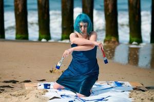 artistieke blauwharige vrouwelijke performancekunstenaar besmeurd met gouacheverf op groot doek op strand foto