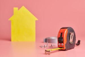 metalen meetlint grappig concept. renovatie huis. huisreparatie en opnieuw ingericht concept. gele huis vormige figuur op roze achtergrond. foto