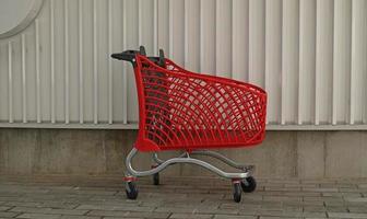 leeg rood boodschappen doen Aan industrieel muur achtergrond. winkel trolley Bij supermarkt. uitverkoop, korting, shopaholisme, zwart vrijdag, economie concept. klant maatschappij tendens. online boodschappen doen concept. foto