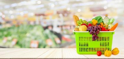 winkelmandje gevuld met fruit en groenten op houten tafel met supermarkt supermarkt wazig onscherpe achtergrond met bokeh licht foto