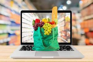 supermarkt gangpad wazig achtergrond met laptop computer en groen boodschappen doen zak Aan hout tafel kruidenier online concept foto